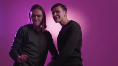 Funny men. Happy celebration. Neon light portrait. Joyful hipster guys dancing snapping fingers on purple white lens flare background slow motion.