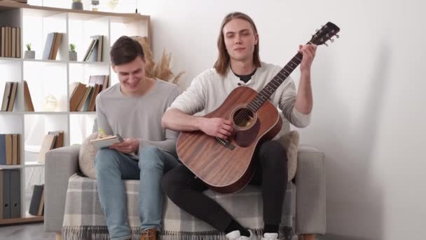 창의적 작곡가 집에서의 남자가 기타를 연주하고 친구가 가벼운 실내에서 필기를 — 비디오