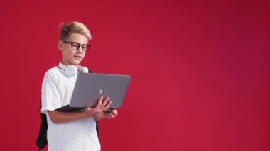 Online meeting. Smart boy. Virtual education. Happy schoolboy talking laptop holding hands posing red background copy space.
