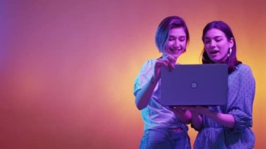 Dijital proje. Heyecanlı kadınlar. Neon ışığı insanları. Şaşırmış kadın arkadaşının bilgisayarını açtı. Mor turuncu arka plan fotokopi alanı oluştururken çok şaşırdı..