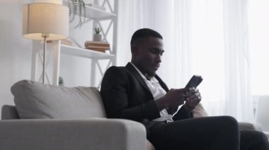 Mobile browsing. Office man. Wireless business. Serious male entrepreneur chatting online texting message on smartphone on sofa.