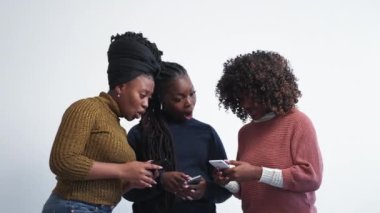 Mobile technology. Female discussion. Digital news. Inspired black women talking about information in smartphones posing light background.