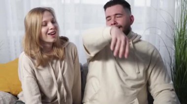 Home relax. Beloved couple. Family leisure. Relaxed man embracing woman sitting together on sofa in light room interior.