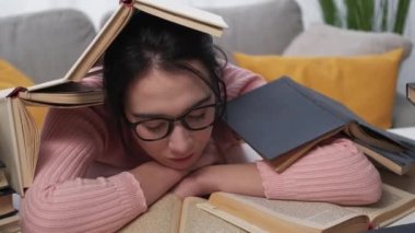 Exhausted education. Sleeping woman. Hard morning. Tired female student waking up sitting desk covering with pile of books in light room interior.