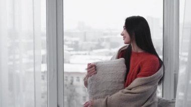 Home leisure. Relaxed woman. Enjoying morning. Happy female sitting on window sill looking outdoor covering plaid in light room interior.