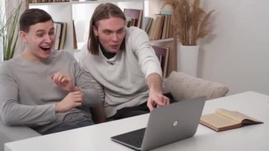 Interesting video. Expressive men. Ridicule fun. Laughing male friends discussing information seeing laptop with skeptic attitude in light room interior.