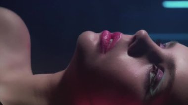 Dikey video. 90 'ların modeli. Moda makyajı. Disko güzeli. Sanatsal görünümlü kendine güvenen genç bir kız yüzü. Kırmızı mavi renkte poz veriyor. Koyu renk üzerinde neon ışıklı..