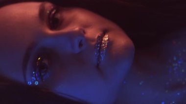 Dikey video. Neon portresi. Parlak makyaj. Gece kulübü güzeli. Pembe mavi renkli, açık renkli, parlak tenli, koyu renk dudaklı kadın yüzü..