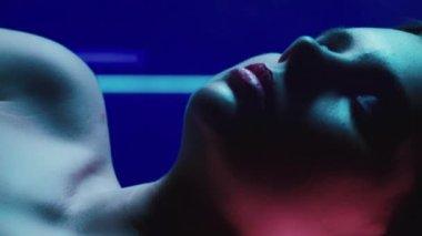 Dikey video. 90 'ların görünüşü. Neon modası. Disko 2000 'in güzelliği. Artistik makyajlı, kapalı gözlü, koyu renk üzerinde kırmızı mor renkte parıldayan rahat genç kız modelinin yakın çekimi..