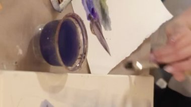 Vertical video. Watercolor painting. Art process. Creative occupation. Closeup of female artist hand using paintbrush color palette creating artwork on paper.