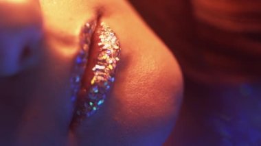 Vertical video. Glitter lips. Neon light girl. Glamour beauty. Cropped closeup of red blue color glow woman face with artistic makeup shimmering metallic skin on dark.
