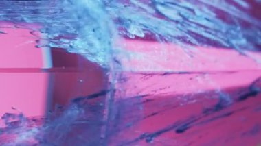Vertical video. Paint splash. Glitter drip. Pyramid cascade. Defocused blue color sparkling ink fluid shot motion on pink glass cube angle abstract background.