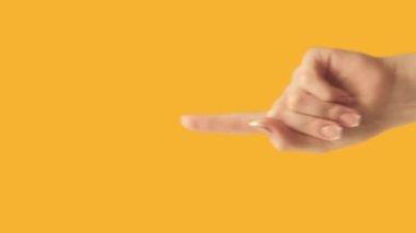 Vertical video. Attention gesture. Information here. Female hand recommending finger pointing up at yellow empty space promotional background.