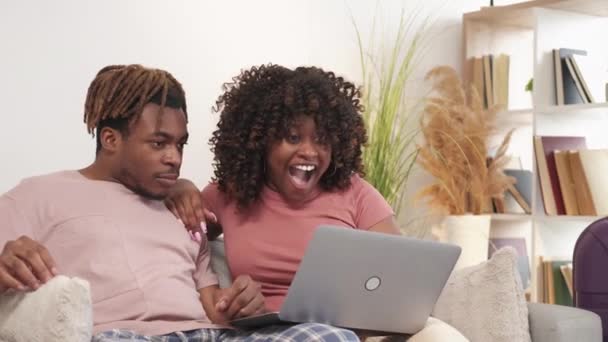热火朝天兴奋的夫妇 网上门票 一个有表情的黑人男人和女人坐在明亮的房间里 坐在沙发上 感觉很快乐 — 图库视频影像