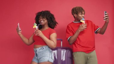 Seyahat fotoğrafı. Mutlu bir çift. Tatil anıları. Mutlu siyah adam ve kadın bavulla selfie çekiyorlar ve kırmızı arka planda akıllı telefonlardan kokteyl yapıyorlar..