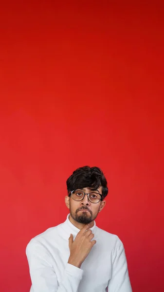 Puzzled man question face. Problem solution. Portrait of astonished confused pensive guy thinking on red color empty space background.