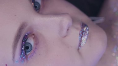 Vertical video. Glitter face. Artistic makeup. Nightclub look. Closeup of glamour woman with sparkling skin metallic eyeshadow lips in blue neon color light.