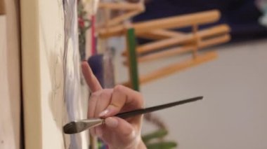 Vertical video. Painting hobby. Art inspiration. Creative talent. Closeup of female artist hand using brush creating watercolor artwork on canvas at workplace.