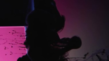 Vertical video. Ink splash. Paint water. Smog cloud. Black fluid motion on pink blue color neon light ice cube angle in water on dark abstract background.
