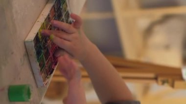 Vertical video. Kid hobby. Finger painting. Out-of-school activities. Unrecognizable talented inspired girl creating picture with watercolor paint on easel in workshop.