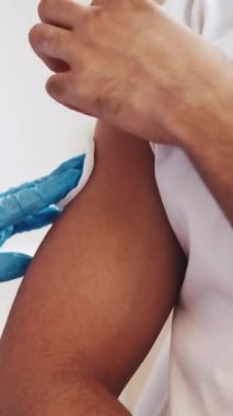 Dikey video. Grip aşısı. Aşı aşısı. Virüs önleme. Doktor eldiven takıp şırınga kullanıyor. Erkek hastanın omzuna iğne saplıyor..