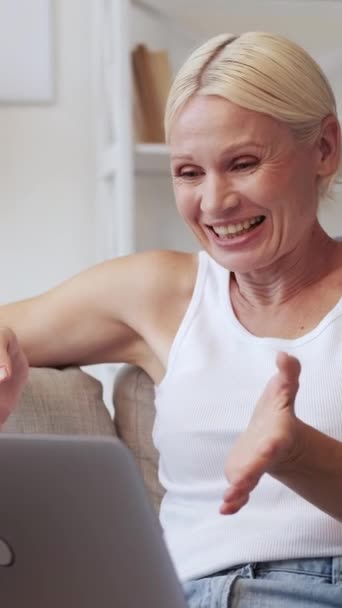 垂直视频呼叫 网络聊天 在线交流 在家里的沙发上使用笔记本电脑 放松快乐快乐的老年女性挥挥手 享受网上聊天的乐趣 — 图库视频影像