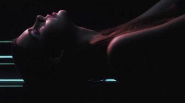 Vertical video. 90s fashion. Night model. Retro look. Profile silhouette of confident teen girl face posing in blue color neon light on dark black.