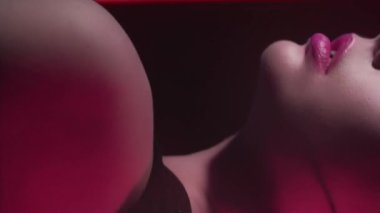 Vertical video. 90s fashion. Neon beauty. Disco look. Cropped profile of confident teen girl model face posing in red pink color flash light on dark.