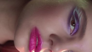 Vertical video. 90s makeup. Retro look. 2000s fashion. Closeup portrait of teen girl face with purple color eyeshadow pink lips artistic visage.