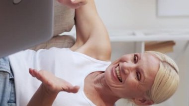 Dikey video çağrısı. İnternet sohbeti. Çevrimiçi iletişim. Rahatlamış, mutlu, mutlu, son sınıf kadını evdeki kanepede dizüstü bilgisayar kullanarak çevrimiçi eğlenceli sohbetler yapıyor..