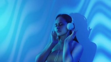 Müzik aşığı. Sakin bir kadın. Çifte portre. Kulaklıklı siluet kadın huzur ve ahenk hissediyor mavi ışık pozu veriyor dalga deseni arka planda.