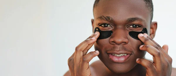 眼斑面部治疗 抗老化护肤 浅空背景下应用黑色保湿面部皮肤凝胶垫化妆品的人的特写肖像 — 图库照片