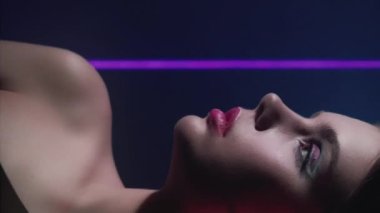 Vertical video. Retro fashion. 90s model. 2000s beauty look. Profile of confident teen girl face with artistic makeup posing in purple blue color neon flash light on dark.