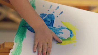 Vertical video. Kid art. Hand painting. Creative imagination. Unrecognizable inspired small girl fingers creating blue yellow color abstract artwork on easel.