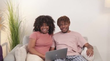 Ev tatili. Aile çifti. Dijital hayat. Mutlu siyahi adam ve kadın dizüstü bilgisayarın aydınlatma odasının içinde birlikte oturup dinleniyorlar..