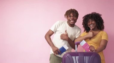 İyi tatiller. Sevgili çift. Yolculuk hazır. Neşeli siyah adam ve kadın jest yapıyor bavul gibi ve pembe arkaplan fotokopi alanı üzerinde biniş kartları.