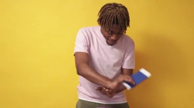 Tatil heyecanı. Mutlu siyah adam. Keyifli yolculuklar. Neşeli stil adamı pasaport ve biletle dans ediyor sarı arka planda ağır çekimde.