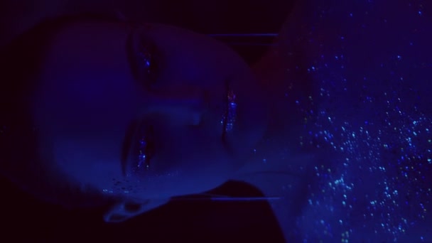 垂直ビデオ ネオンの肖像画 キラキラした肌 パーティーの様子だ 青い紫色のライト女性顔ともに芸術的なメイクキラキラアイシャドウ唇でミラーオンダーク — ストック動画