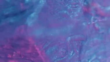 Vertical video. Neon fluid. Ink splash. Sparkling frost. Defocused blue pink color light glitter paint drop motion on cube edge in water abstract background.