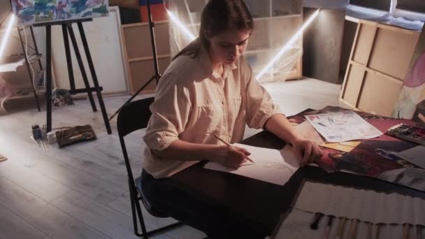 アートスタジオ 女性を描く アート作品制作 濃密女性座ってテーブルスケッチ女性の肖像画で暗い光の部屋のインテリア — ストック動画
