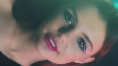 Vertical video. Retro makeup. 90s beauty. 2000s nostalgia. Cheerful teen girl fashion model face with blue color eyeshadow pink lips artistic look posing in neon light on dark.