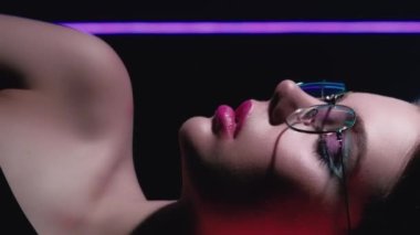 Vertical video. 90s look. Retro fashion. 2000s beauty. Profile portrait of teen girl face with artistic makeup wearing glasses posing in red purple blue color neon light on black.