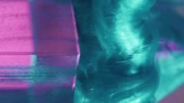Vertical video. Ink splash. Paint water. Explosion fume. Defocused green pink color glitter fluid flow smoke cloud motion over neon light glass cube angle abstract background.