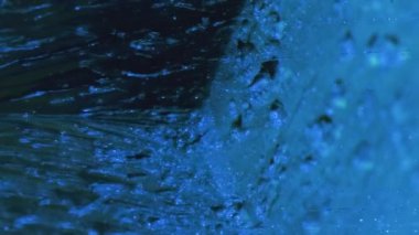 Vertical video. Paint drip. Glitter fluid. Ice cascade. Blue color sparkling flakes texture ink fall motion on cube angle abstract background.