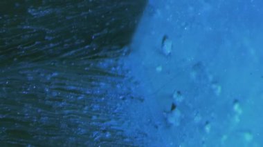 Vertical video. Glitter fluid. Ink flow. Ice cascade. Blue color sparkling grain texture liquid drip motion on cube angle dark abstract background.