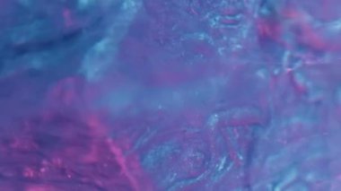 Vertical video. Neon fluid. Ink splash. Sparkling frost. Defocused blue pink color light glitter paint drop motion on cube edge in water abstract background.