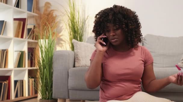 望まない妊娠だ 落ち込んでる女性 携帯電話だ 悲しい黒の女性が話してスマートフォン保持テスト結果座って床の光部屋のインテリア — ストック動画