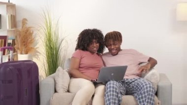 Turne seçiyorum. İlham verici bir çift. Çevrimiçi sipariş. Mutlu siyah erkek ve kadın, dizüstü bilgisayarda yolculuk arayan keyifli bir şekilde kanepede, aydınlık odada oturuyor..