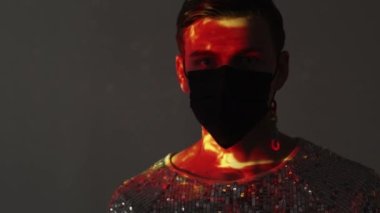 Şık bir görünüş. Lgbtq erkek portresi. Güvenlik dursun. İpek gömlekli eşcinsel adam, siyah koruyucu maske takıyor. Gri arka plan, çift pozlu gün batımı ışığı yansıtma lensini yansıtıyor..