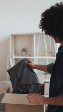 Dikey video. Eşyaları yerleştiriyorum. Ev taşınması. Evi değiştir. Yeni apartman dairesinde kaplanmış mobilyalarla karton kutudan kıyafet ayarlayan mutlu adam..